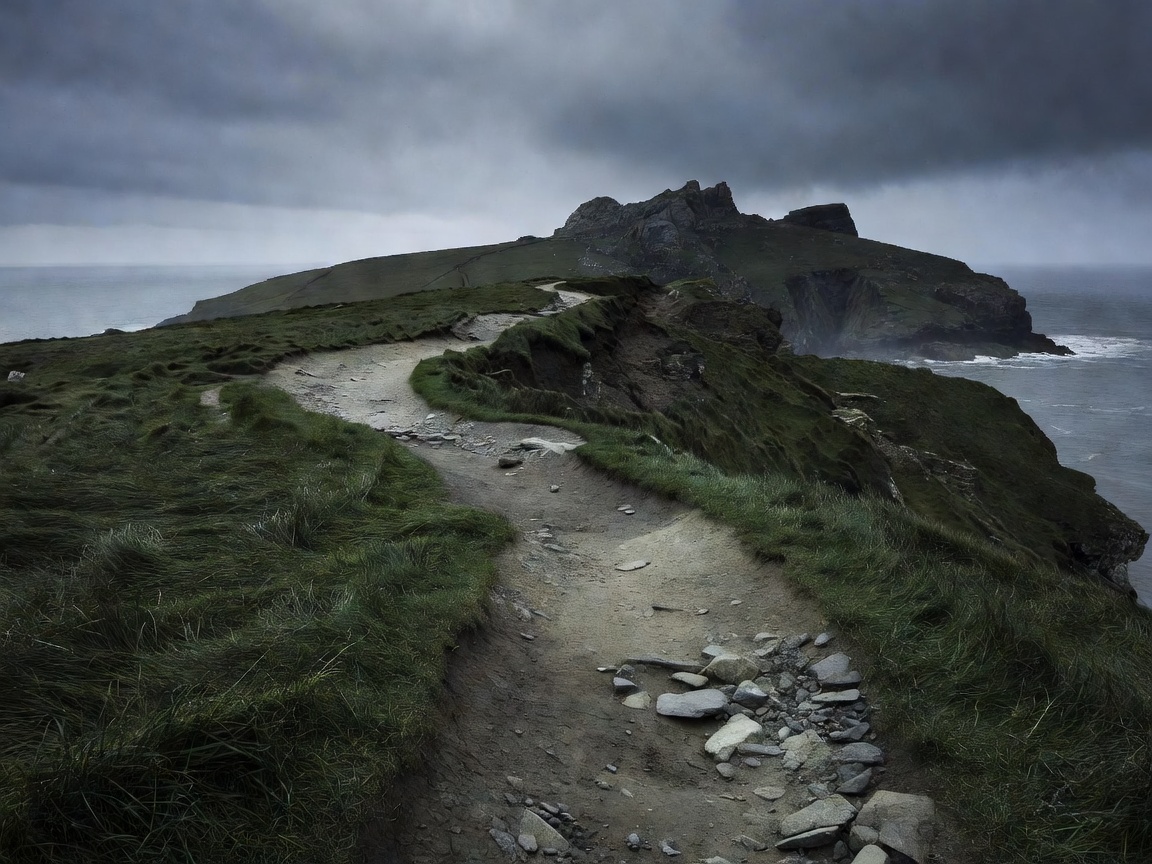 A narrow coastal path curving through dark grass toward a distant headland